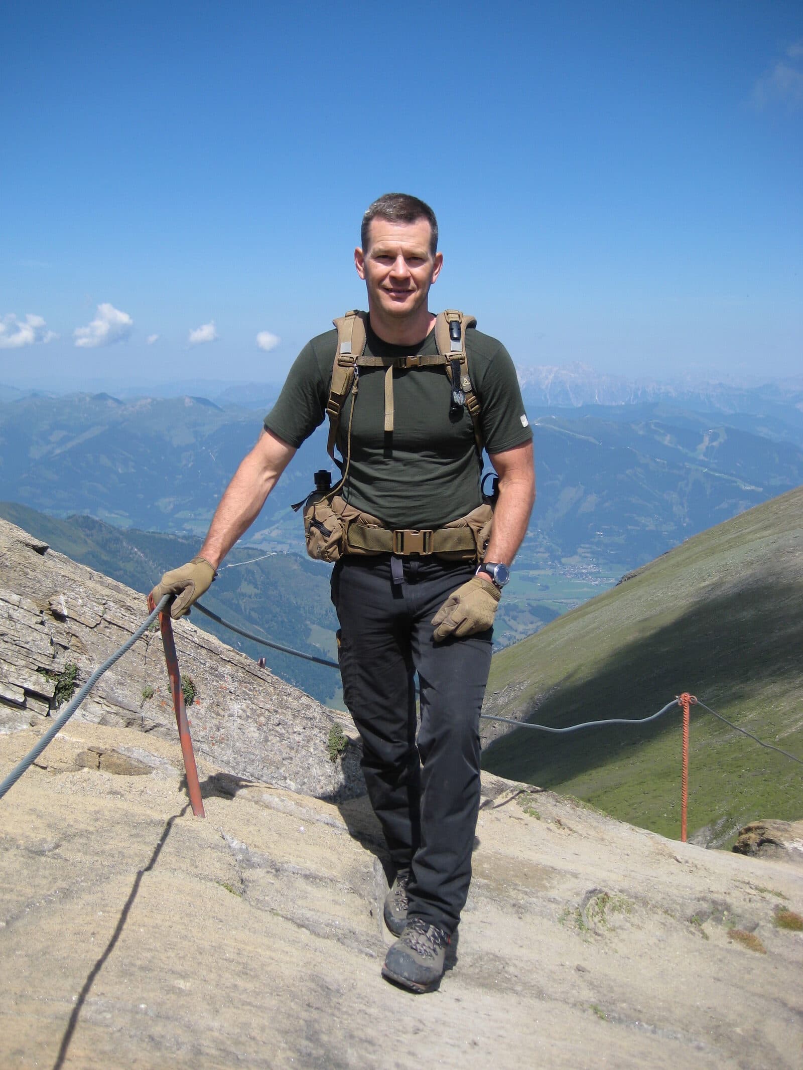 Kenneth Bolyard carrying a pack on a secured mountain path high above an alpine valley